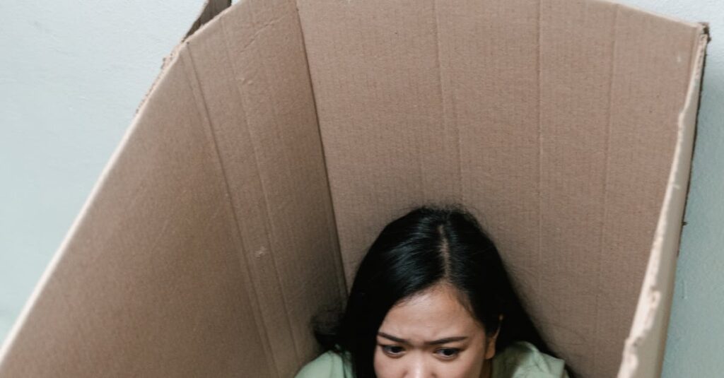 A woman sits inside a cardboard box appearing anxious, symbolizing feelings of claustrophobia.